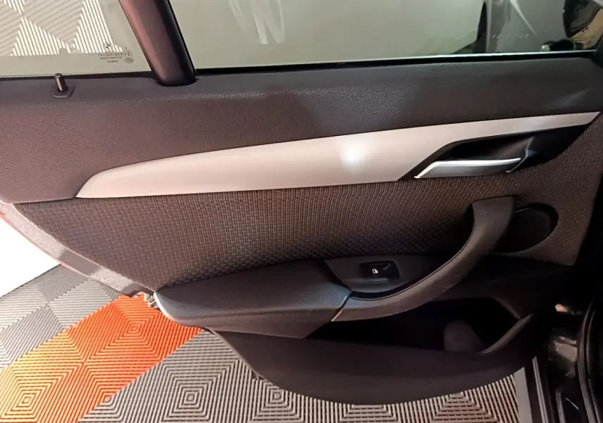 Vue rapprochée de la porte arrière gauche noire d’un BMW X1 2020 avec poignée et bouton de verrouillage intégré.