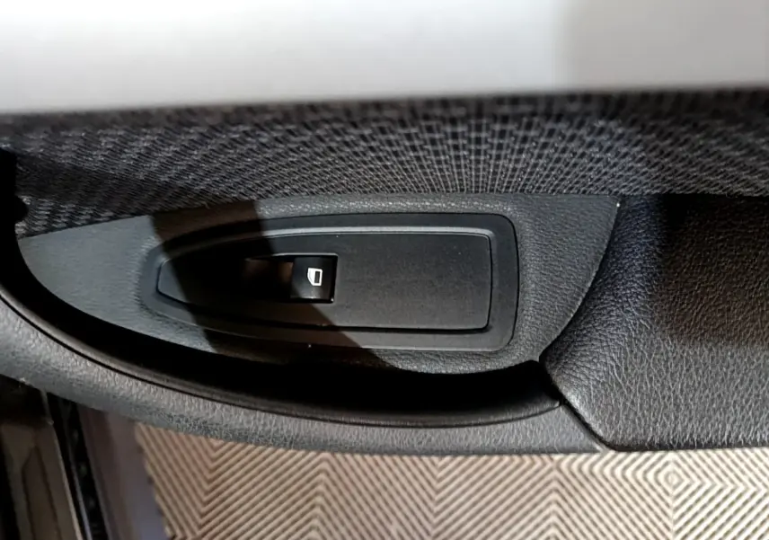 Gros plan sur le bouton de commande de la vitre électrique côté conducteur d'un BMW X1 noir.