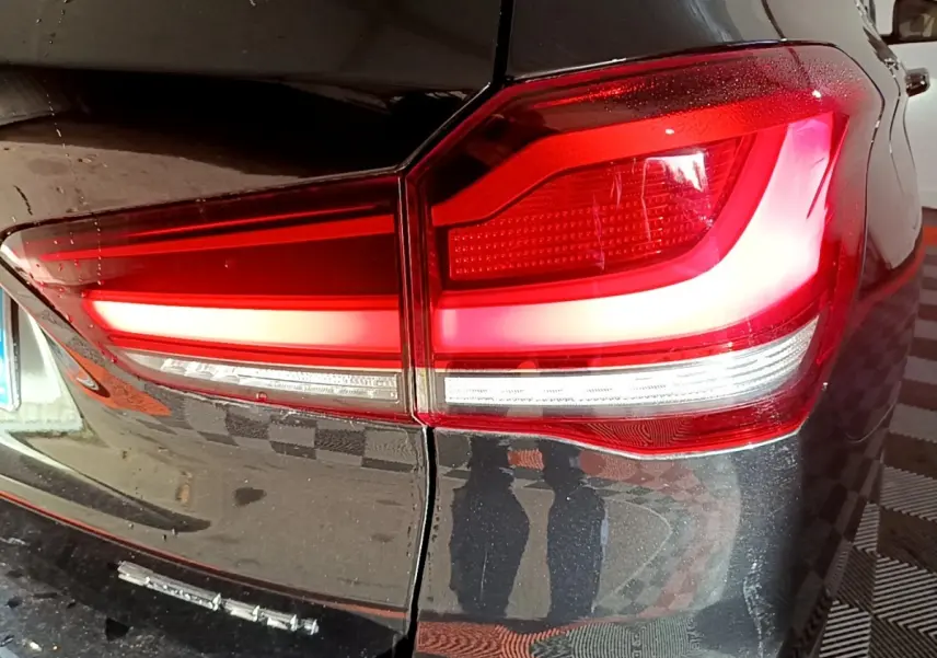 Gros plan sur le feu arrière droit rouge et blanc d’un BMW X1 noir, avec reflet sur la carrosserie brillante.