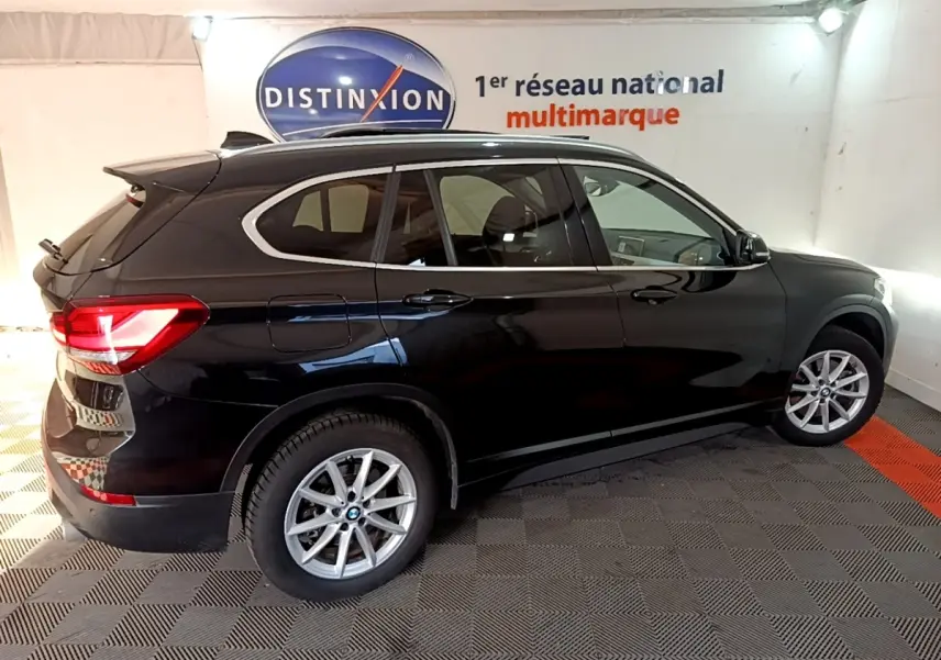 BMW X1 noir vue de profil côté droit dans un showroom avec jantes alliage et feux arrière allumés.