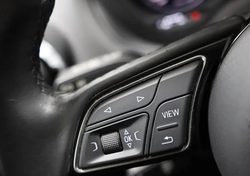 Gros plan sur les commandes au volant en cuir noir de l'Audi Q2 gris, avec boutons de navigation et fonction View.