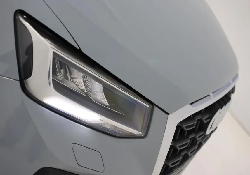 Gros plan sur le phare avant droit gris d'un Audi Q2 2023, mettant en valeur la calandre hexagonale et les lignes nettes.