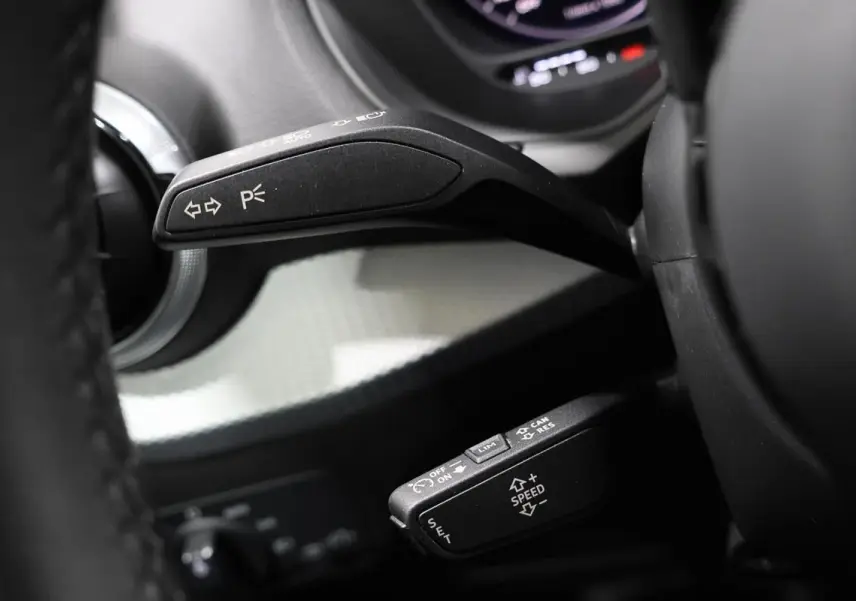Gros plan sur les commandes au volant d’un Audi Q2 gris 2023, mettant en valeur les leviers de clignotants et régulateur de vitesse.
