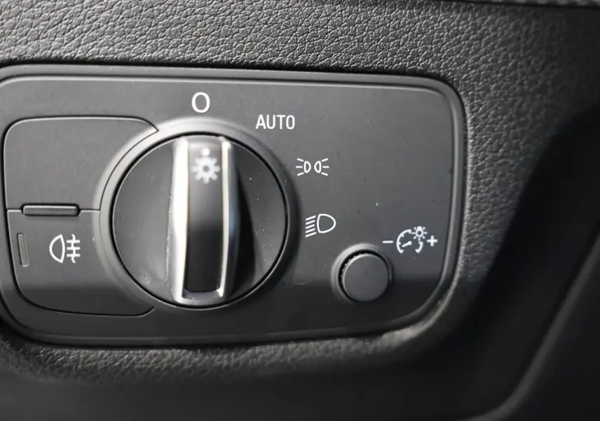 Gros plan sur le bouton de commande des phares de l'Audi Q2 gris, situé sur le tableau de bord côté conducteur.
