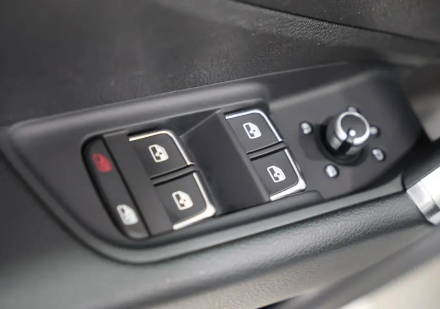 Gros plan sur les commandes de lève-vitres et réglage des rétroviseurs côté conducteur de l'Audi Q2 gris 2023.