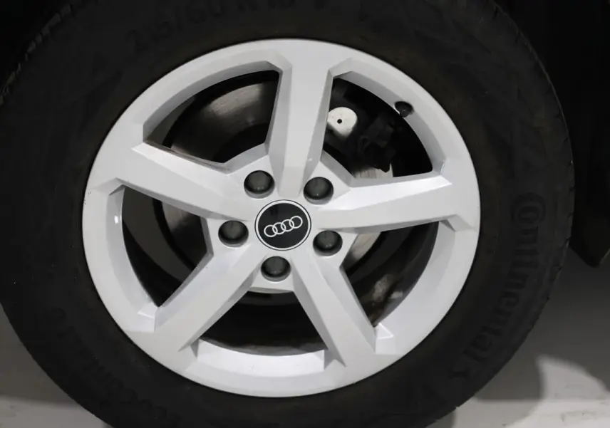 Gros plan sur la jante blanche à cinq branches d’un Audi Q2 gris, mettant en valeur le logo Audi au centre.