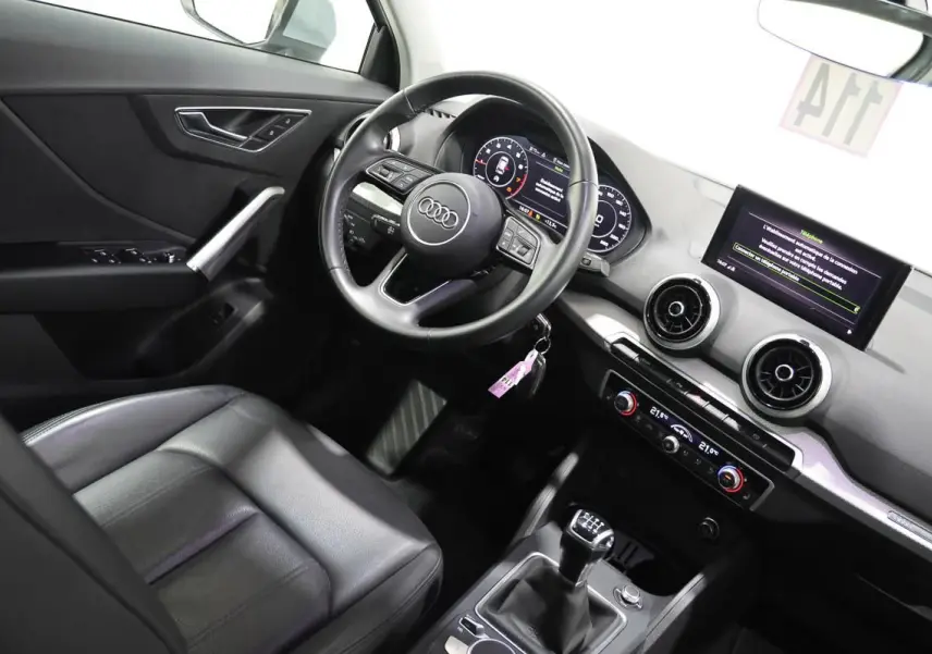 Vue intérieure côté conducteur de l'Audi Q2 gris, volant cuir, écran digital et sièges cuir chauffants visibles.
