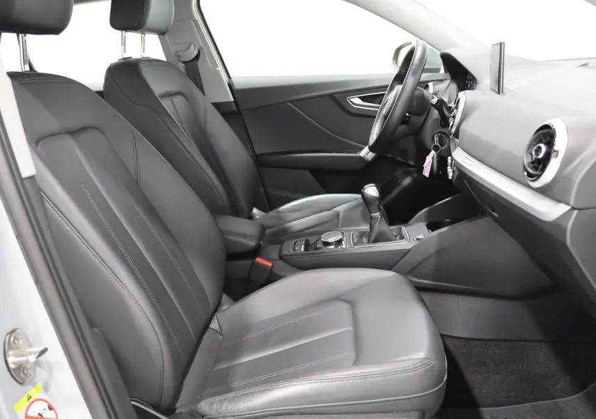 Vue intérieure côté conducteur de l'Audi Q2 2023, sièges cuir noirs et tableau de bord avec écran GPS escamotable.