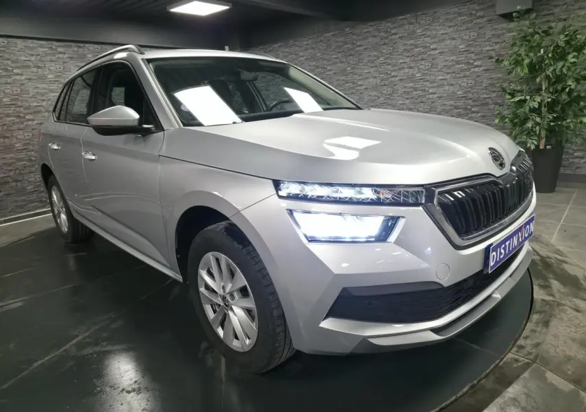 Vue 3/4 avant droit d'un Skoda Kamiq gris métallisé avec feux LED allumés dans un showroom intérieur.