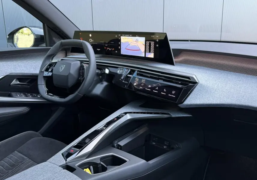 Vue intérieure côté conducteur du Peugeot 5008 Hybrid 2026, mettant en valeur le tableau de bord moderne avec écran incurvé et sellerie Alcantara grise.