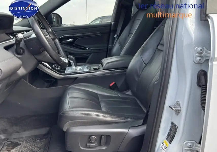 Vue intérieure côté conducteur du Range Rover Evoque blanc, mettant en valeur les sièges cuir noirs et l'accoudoir central.