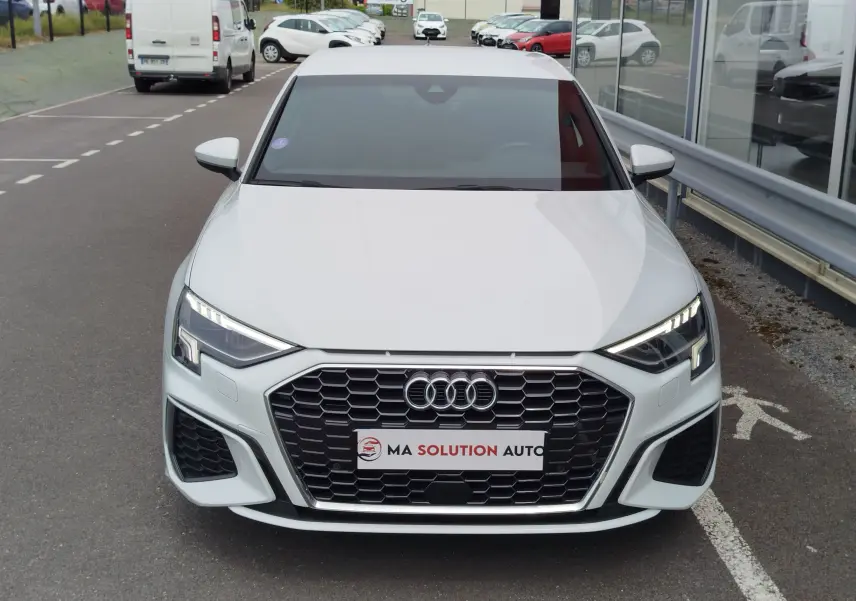 Vue frontale d'une Audi A3 Sportback blanche Glacier métallisé avec calandre hexagonale et phares LED allumés.