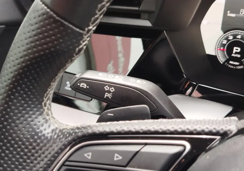 Gros plan sur le commodo de clignotant noir et le volant perforé de l'Audi A3 Sportback blanc Glacier 2022, intérieur moderne.
