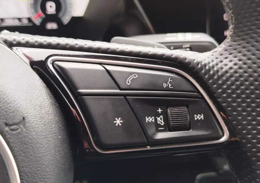 Gros plan sur les commandes multifonctions noires du volant perforé de l'Audi A3 Sportback blanc Glacier 2022.