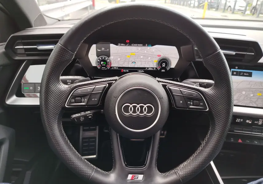 Vue centrée sur le volant cuir perforé de l'Audi A3 Sportback 30 TFSI S line avec tableau de bord numérique allumé.