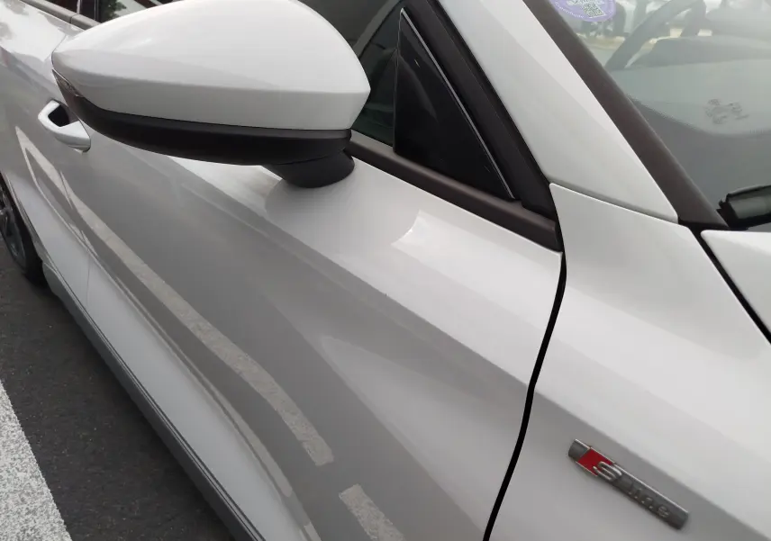 Vue rapprochée du côté gauche avant de l'Audi A3 Sportback blanc Glacier avec badge S line sur la portière.