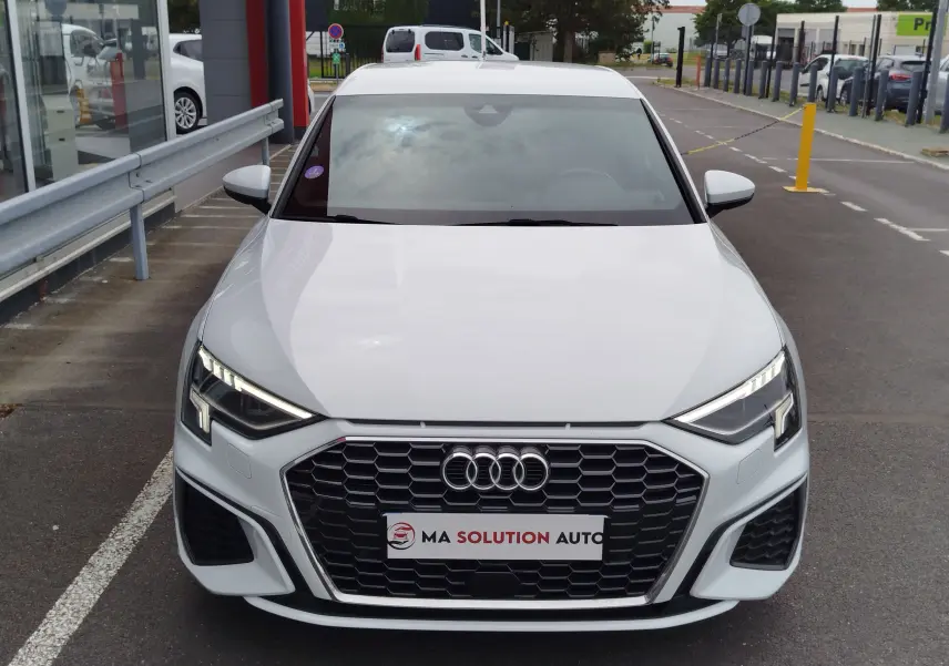 Vue avant d'une Audi A3 Sportback blanc glacier métallisé avec calandre hexagonale noire et phares LED allumés.