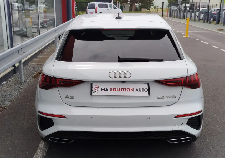 Vue arrière d'une Audi A3 Sportback blanc glacier métallisé avec feux LED et double sortie d'échappement intégrée.