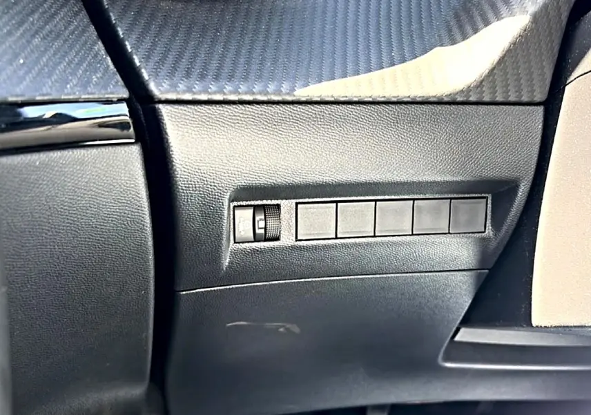 Détail intérieur côté conducteur du tableau de bord noir avec commande de réglage de phares sur Peugeot 2008 gris 2025.