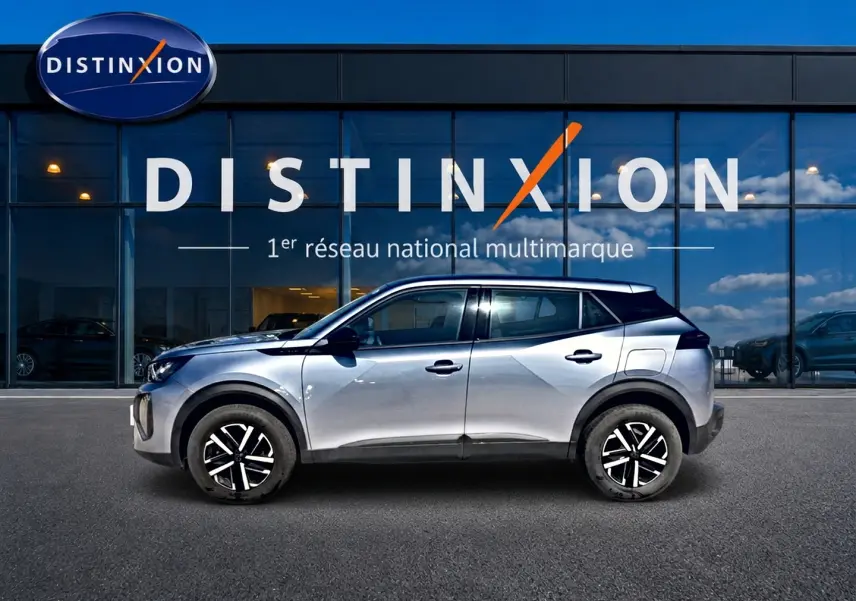 Peugeot 2008 gris en profil droit, avec toit noir et jantes noires à motifs blancs, devant une vitrine Distinxion.