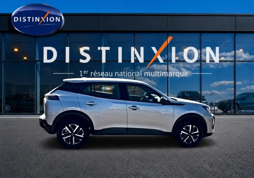 Profil côté gauche d'un Peugeot 2008 gris 2025 avec jantes noires et toit blanc devant une vitrine Distinxion.