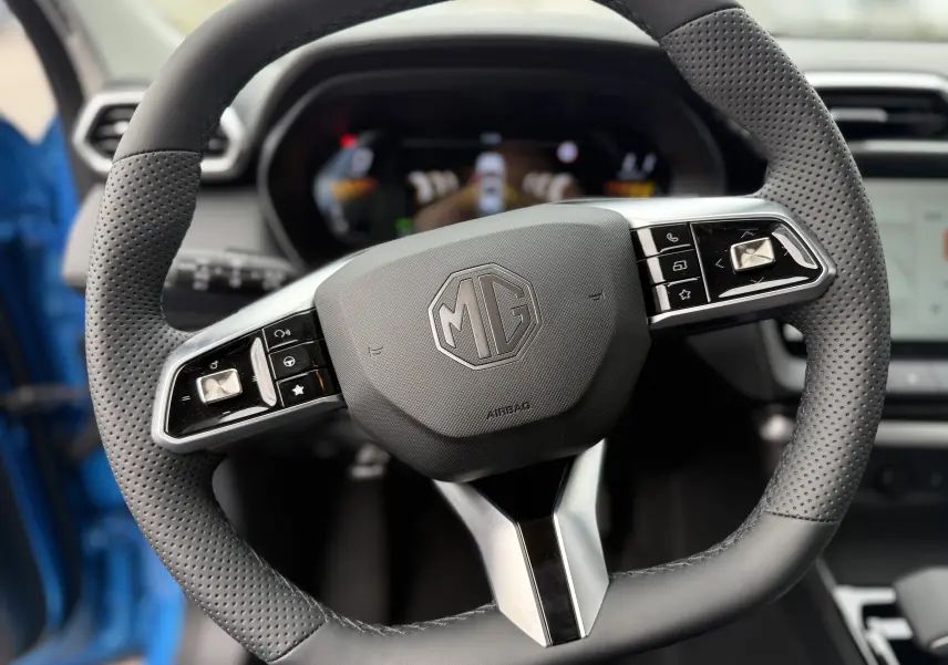 Gros plan sur le volant en cuir perforé du MG ZS 1.5 Hybrid+ 197 Luxury, avec commandes intégrées et logo MG central.