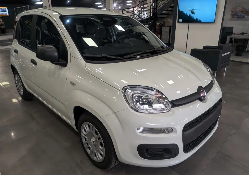 Vue 3/4 avant d'une Fiat Panda 1.0 70 CH Hybrid City blanche Gelato en showroom, avec rétroviseurs noirs et jantes acier.