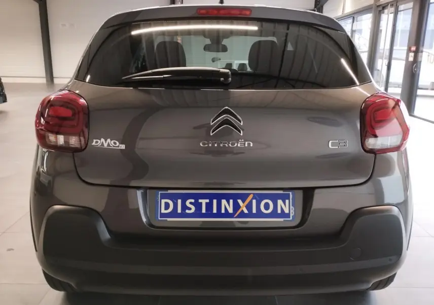 Vue arrière d'une Citroën C3 gris foncé 2024 avec feux arrière arrondis et pare-chocs noir mat en intérieur showroom.