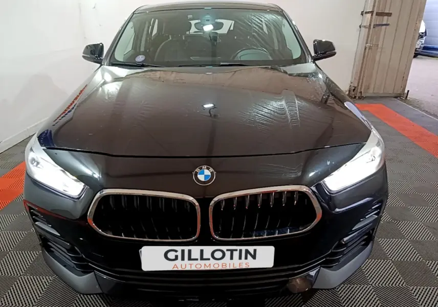 Vue avant d'un BMW X2 sDrive18i Lounge noir avec phares LED allumés dans un garage.
