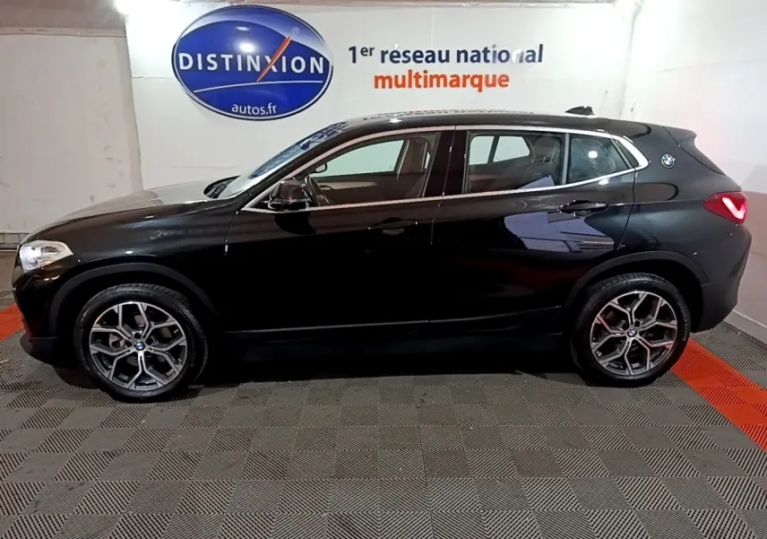 BMW X2 sDrive18i Lounge noir vue de profil côté gauche, avec jantes alliage et logo BMW sur l'aile arrière.
