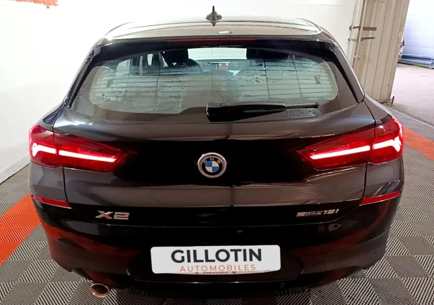 Vue arrière d’un BMW X2 sDrive18i noir avec feux LED allumés et logo visible sur fond intérieur showroom.