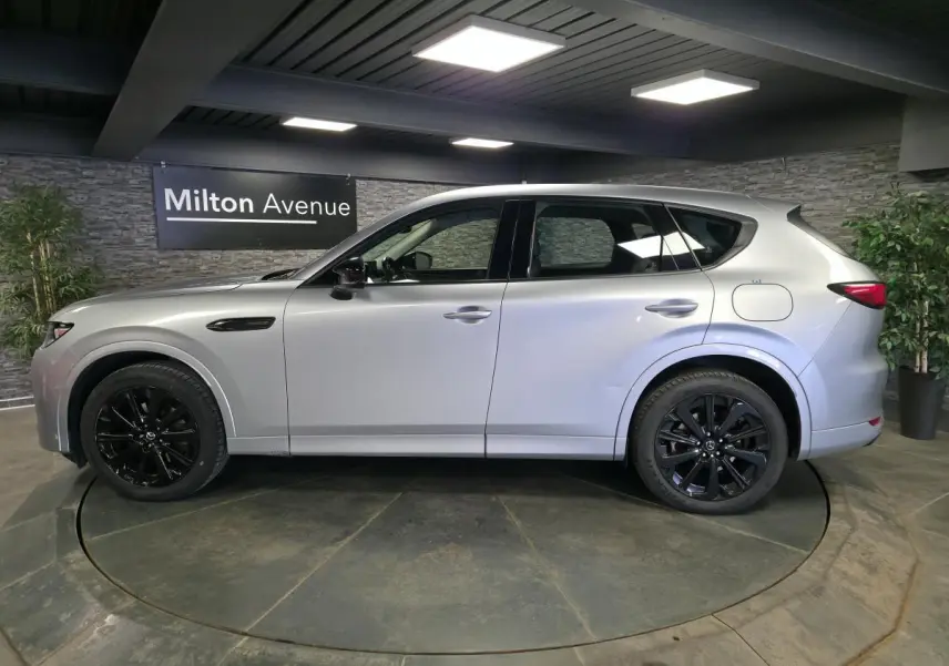 Vue latérale droite du Mazda CX-60 gris Sonic Silver avec jantes alliage noires dans un showroom intérieur.