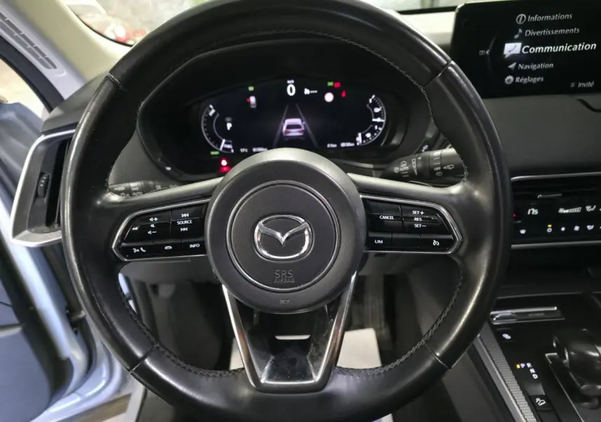 Vue frontale du volant cuir noir du Mazda CX-60 gris avec commandes intégrées et tableau de bord numérique allumé.