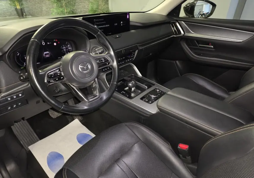 Intérieur avant du Mazda CX-60 gris, vue côté conducteur, volant cuir noir et console centrale avec écran tactile.