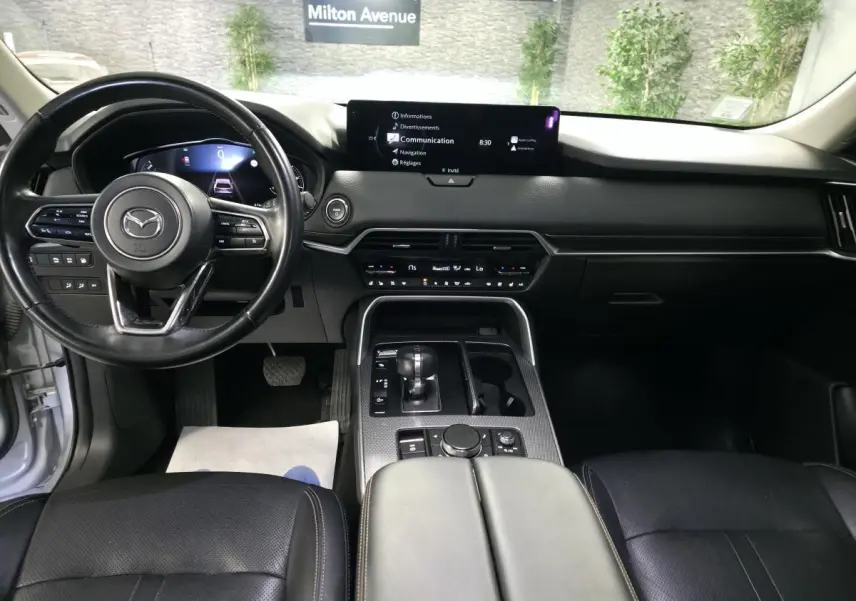 Vue intérieure avant du Mazda CX-60 gris, tableau de bord noir avec écran central large et volant cuir multifonction.