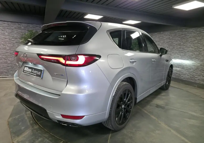 Vue 3/4 arrière droite du Mazda CX-60 gris Sonic Silver avec jantes noires et feux arrière LED allumés.