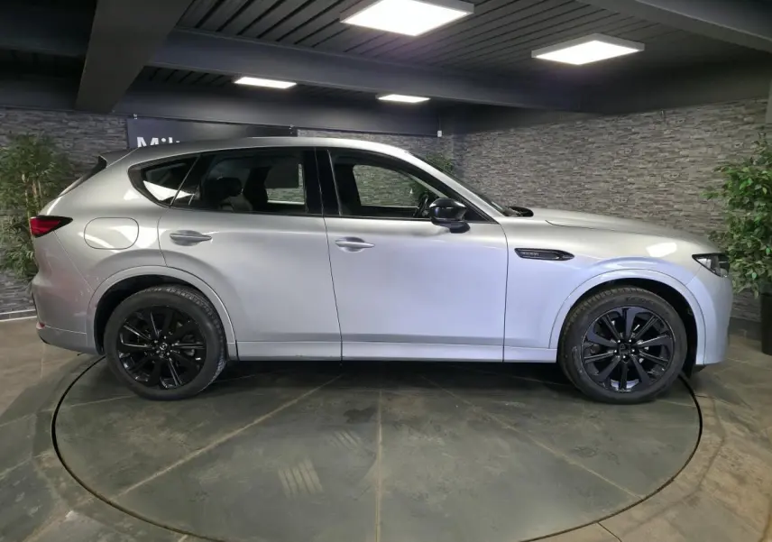 Vue latérale droite du Mazda CX-60 gris Sonic Silver avec jantes alliage noires dans un showroom intérieur.