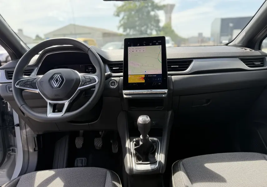 Vue intérieure frontale du tableau de bord du Renault Captur 2025 avec écran tactile vertical et levier de vitesse manuel.
