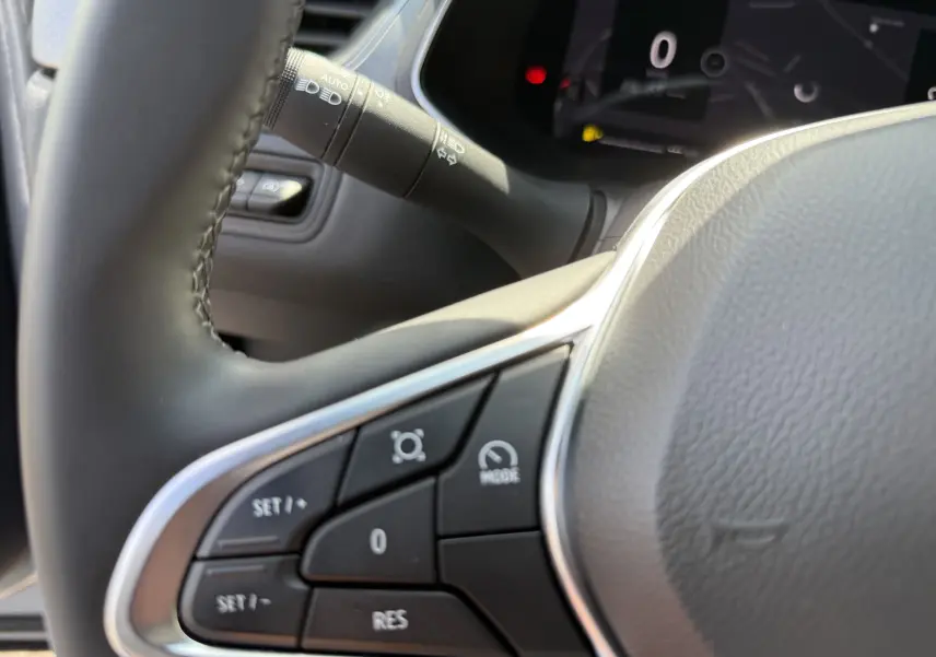 Gros plan sur les commandes au volant à gauche du Renault Captur 2025 gris rafale avec toit noir, affichage digital en arrière-plan.
