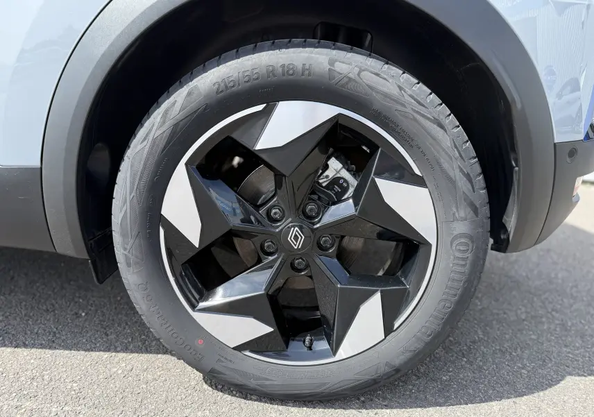 Gros plan sur la roue avant droite du Renault Captur 2025 gris Rafale avec jante noire et argentée au design géométrique.