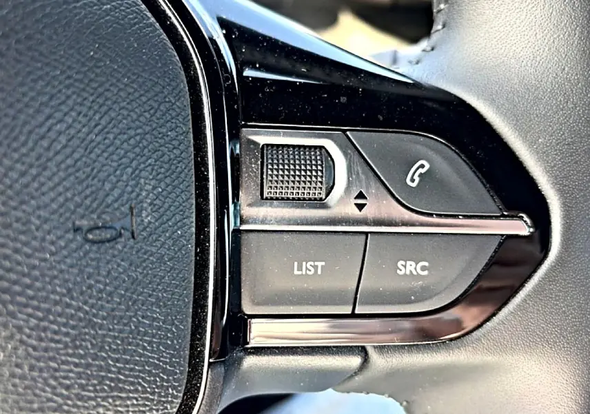 Gros plan sur les commandes gauche du volant noir du Peugeot 2008 gris, avec boutons LIST, SRC et téléphone.