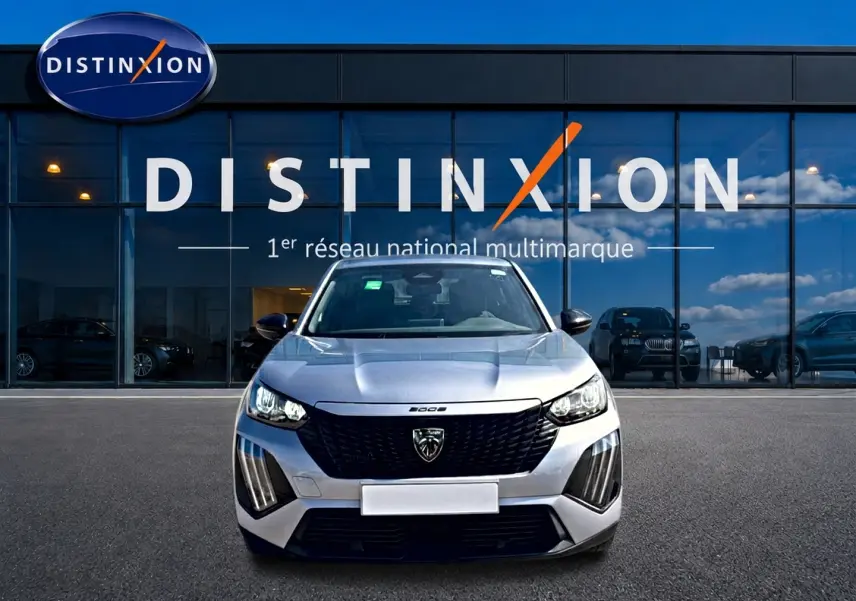 Vue frontale d'un Peugeot 2008 gris 2025 avec calandre noire et feux LED, devant une vitrine Distinxion.
