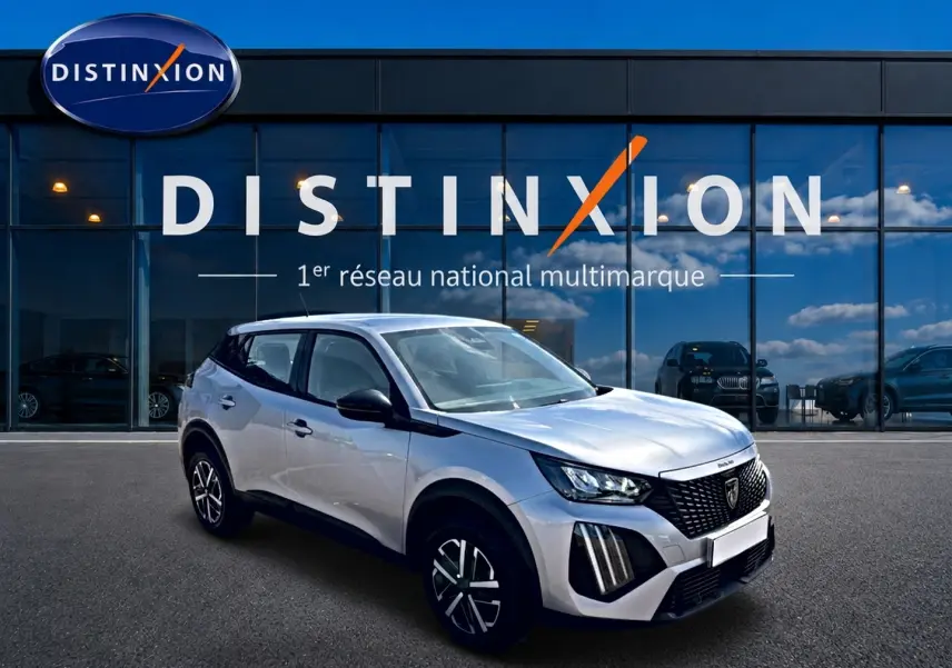 Peugeot 2008 gris en 3/4 avant droit, avec calandre noire et jantes distinctives, devant showroom Distinxion.