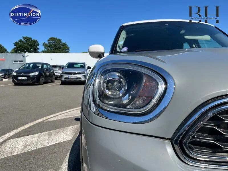 Gros plan sur le phare avant gauche d'une MINI Countryman Moonwalk Grey avec rétroviseur blanc et calandre chromée.