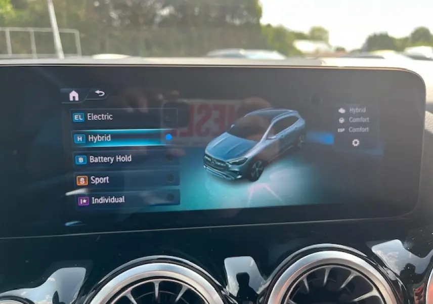 Écran central affichant les modes de conduite d'une Mercedes GLA 250 e hybride, vue 3/4 avant virtuelle grise.
