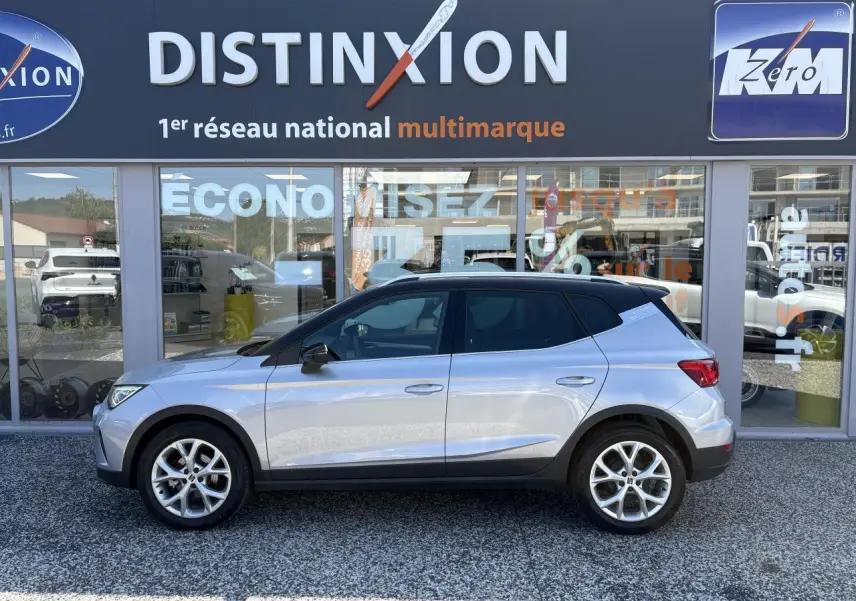 Vue profil côté gauche du SEAT Arona 2024 rouge passion avec jantes alliage 16 pouces devant un showroom Distinxion.