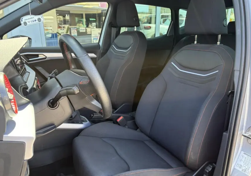 Intérieur avant du SEAT Arona 2024, sièges textile noirs avec surpiqûres rouges et volant sport cuir multifonction.