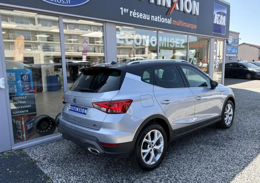Vue 3/4 arrière droite d'un SEAT Arona 2024 gris GRS avec jantes alliage et logo FR devant un showroom.