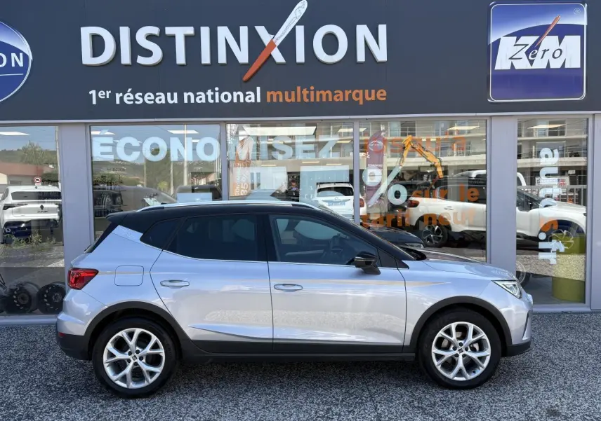 Vue latérale droite d'un SEAT Arona 2024 GRS avec toit noir et jantes alliage 16 pouces devant un showroom Distinxion.