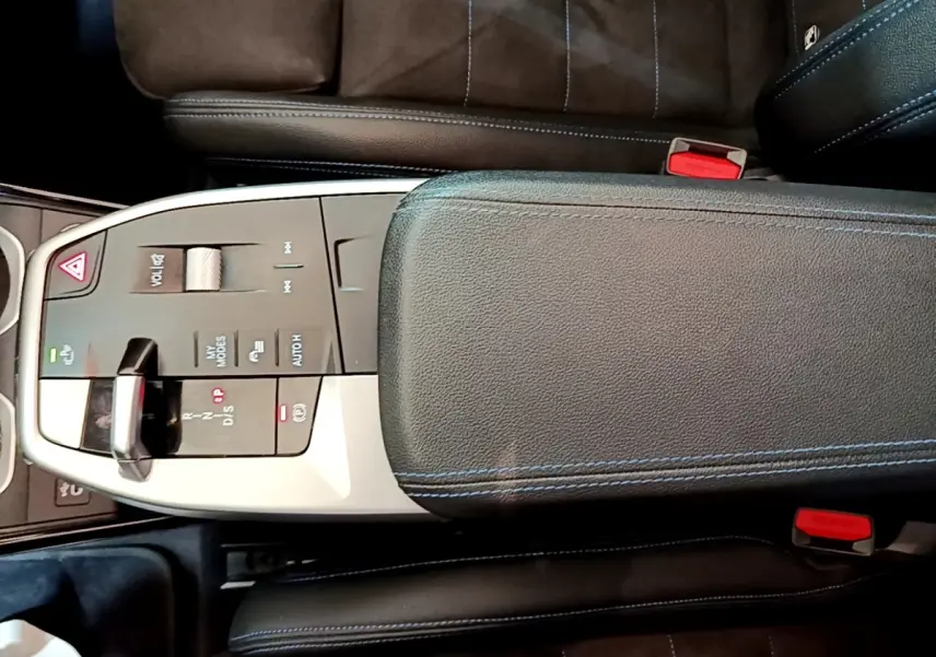 Vue plongeante sur la console centrale noire du BMW X1 xDrive23i M Sport 2023 avec accoudoir et commandes tactiles.